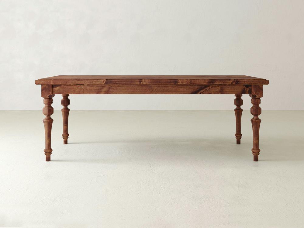 An Allyson Dining Table - Tuscany by James+James, featuring a rustic design with a rectangular top and four turned legs, stands on a light-colored floor. The table showcases a natural wood grain finish against a plain, off-white wall.