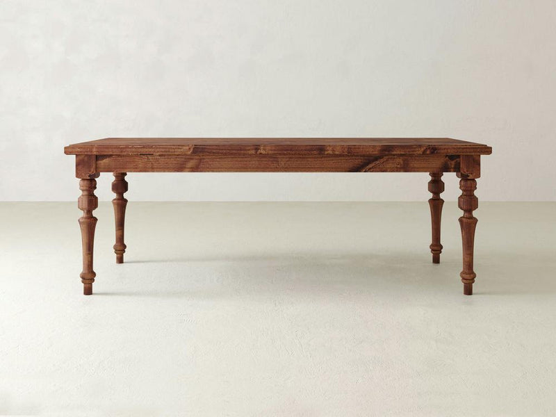An Allyson Dining Table - Tuscany by James+James, featuring a rustic design with a rectangular top and four turned legs, stands on a light-colored floor. The table showcases a natural wood grain finish against a plain, off-white wall.