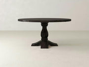 The Heirloom Round Dining Table - Charred Ember by James+James features a smooth, dark wooden surface with a classic design. It stands on a single pedestal leg with four feet and is set against a light-colored background, offering a simple yet elegant appearance.