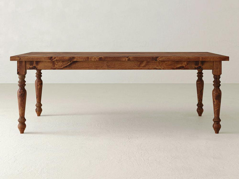 A James+James French Country Dining Table - Tuscany, crafted with sturdy wood and a rich brown finish, featuring intricately carved legs and a smooth rectangular top. The table is set against a plain, light-colored background.