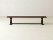 The James+James Heirloom Bench - Tobacco on Alder features ornate legs and a support beam, set against a plain white wall on a light floor.