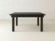 A minimalist, square wooden table in a charred ember finish from James+James, featuring clean lines and a smooth surface, is set against a plain light-colored background. This Farmhouse Square Dining Table has four straight legs and a simple design.