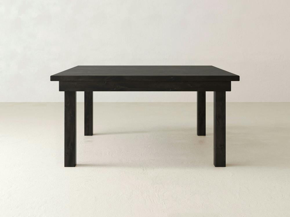 A minimalist, square wooden table in a charred ember finish from James+James, featuring clean lines and a smooth surface, is set against a plain light-colored background. This Farmhouse Square Dining Table has four straight legs and a simple design.