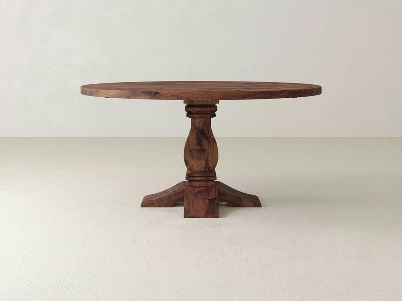 A close-up of the *Heirloom Round Dining Table - Tuscany* by *James+James*, showcasing its wooden surface with a prominent knot in the center. The wood features a rich, warm brown tone complemented by visible horizontal grain patterns. The knot displays a dark, circular appearance with radiating cracks.